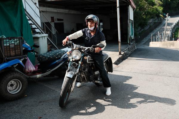 A man on a motorcycle, outside the little supermarket.